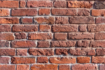 A wall of old, cracked bricks, with a weathered and faded surface. Restored brickwork of an old house.