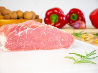 Cut Piece of Pork Loin on white cutting board, raw fresh meat on kitchen table with various ingredients and spices