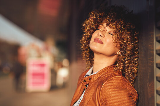 Portrait Of A Young Woman In A Brown Leather Jacket With Blond Afro Curly Hair On The Street