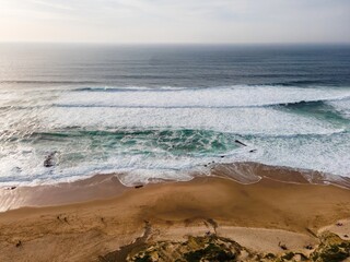 Aerial view of a beautiful Guincho beach with Atlantic Ocean waves rolling on the shoreline at twilight, Cascais, Portugal.