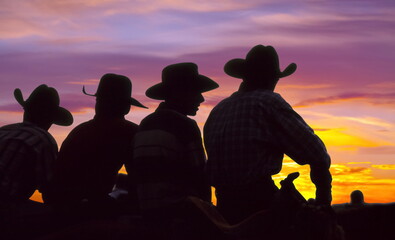 four cowboys looking at the horizon at dusk