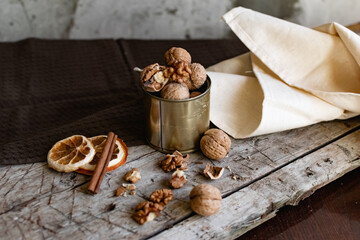 Walnuts in a tin of yellow metal next to the shell and the nuts on the inside. Decorated with dried oranges and a cinnamon stick. Composition of products and food on a wooden Board