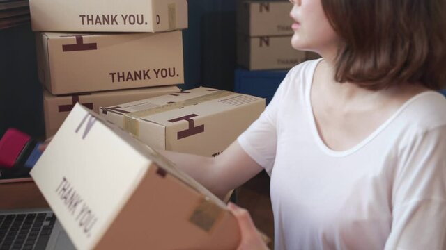 Asian Female seller online store worker holding scanner scanning parcel bar code packing e commerce post shipping box preparing online retail shop order in drop shipping delivery service warehouse.