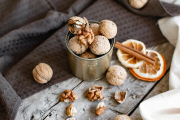 Walnuts in a tin of yellow metal next to the shell and the nuts on the inside. Decorated with dried oranges and a cinnamon stick. Composition of products and food on a wooden Board