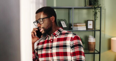 Close up portrait of handsome young African American guy in glasses standing in room near window...