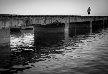 Sorrow. Silhouette of a lonely man on a pier, black and white image. - 418748896