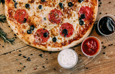 Pepperoni pizza with olives. sprinkled pepper on the table. Three types of sauce