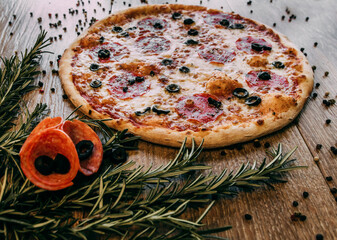 Pepperoni pizza with olives and rosemary branches on the table