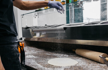 The cook prepares the pizza dough. Sprinkles with white flour