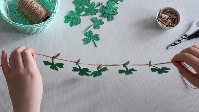 DIY St.Patricks Day decor. Hands make shamrocks garland of glitter paper on white table