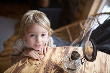 Cute toddler child in a little fancy wooden cottage, reading a book, drinking tea