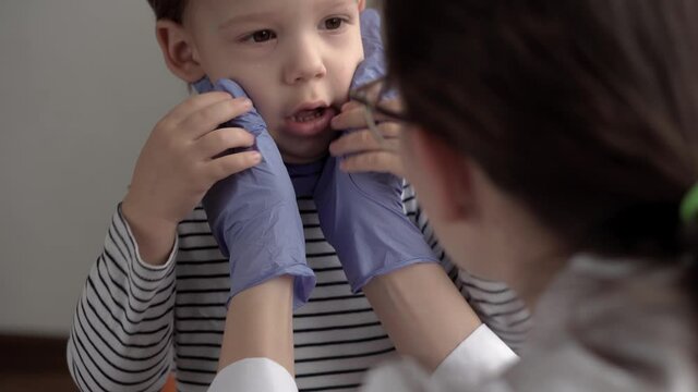 close up woman doctor dermatologist in blue gloves examines face 3-4 years minor preschool boy kid. Over the Shoulder shot nurse treats acne in child. medicine and health, pediatrics, covid-19 concept
