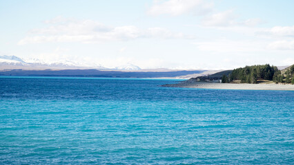 Lake Tekapo with nearby snow covered mountain peaks on a sunny day in the South Island of New Zealand.