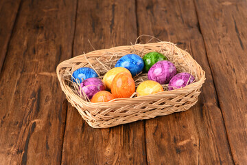 Colorful easter eggs in the basket on a wooden table.