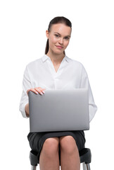 Portrait of attractive young woman in formal clothes isolated on white background sitting on chair and working on laptop. Concept of corporate dress code.