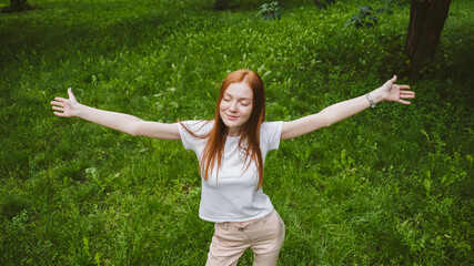 Self care, mental wellbeing, mental health, mindfulness. Young red-haired woman enjoying life in nature among flowers and green trees