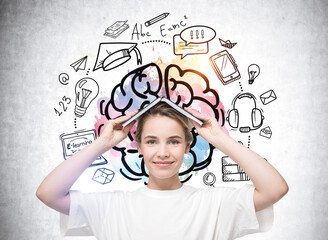 Attractive smart student woman in casual white t-shirt holding open book on head like house. Colorful business education and e-learning sketch drawn on wall behind