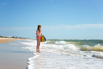 Tween red haired girl in swimsuit with boogie board at the beach.