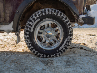 Fototapeta na wymiar A wheel with a beautiful SUV car disc. Winter studded tires on off road. The concept of winter car competitions on ice. The texture of a rubber tire with spikes in the snow.
