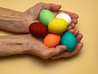 An old, elderly woman holds or gives, holds out multicolored, colored boiled chicken eggs in her wrinkled hands. Traditional elements of a happy Orthodox or Catholic Easter.