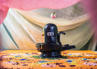 Black handmade Shiva Lingam figure with on an orange altar under curtains with roses