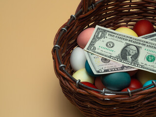Money, dollar bills lie on Multicolored, painted boiled chicken eggs in a wicker wooden, rustic basket. Traditional elements of a happy Orthodox or Catholic Easter. Egg Hunt Concept
