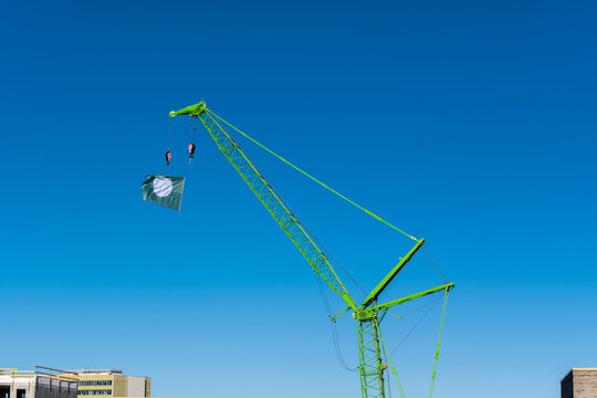 Green crane on a beautiful blue sky. The crane has a white and green flag at the tip, waving in the wind. It is a beautiful sunny spring day.