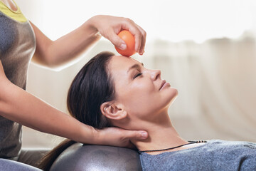 A woman master performs a myofascial massage of the face of a client with a small ball. Concept on...