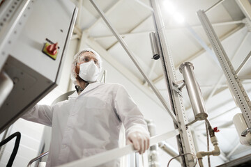 Low angle portrait of male worker operating machines at chemical plant while wearing lab coat and protective clothing, copy space