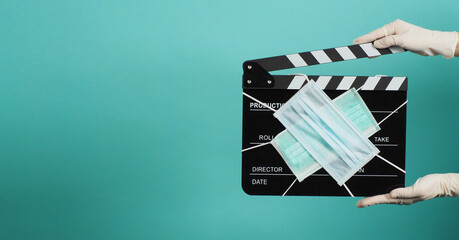Hand is wear white medical gloves and hold black Clapper board or movie slate with face mask. it...