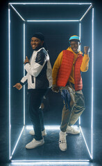Two stylish rappers poses in glowing cube