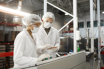 Side view portrait of two workers wearing protective clothing while operating machine units at...