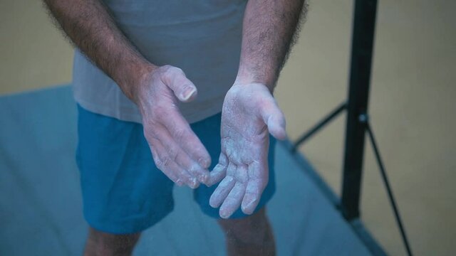 Man in the gym claps his hands soiled with chalk.
Clapping hands form a cloud of chalk dust. Motivation and stranght before the workout.