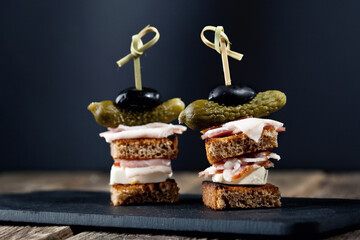 canapes slices of black bread cream bacon pickled cucumbers of olive on a stud on a black shale...