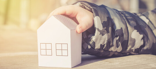 A child's hand holds a paper house in the rays of the sun. New home buying concept