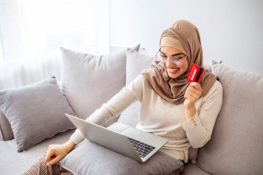 Easy payments. Smiling arabic woman in headscarf using laptop and credit card at home, paying for utilities online, free space. Online Credit Concept.