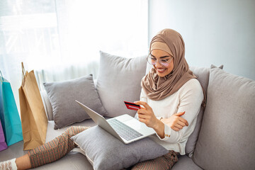 Close up shot of Muslim mother buying groceries online from her laptop at home, paying with credit card, during Coronavirus pandemic. Shot of a young woman using a laptop and credit card at home