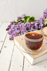 Romantic background with a cup of tea, lilac flowers and a book over a white wooden table. Leisure concept, spring breakfast