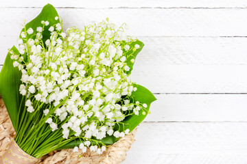 beautiful bouquet of Lily of the valley flowers in a basket on a white wooden background with a copy space close up top view
