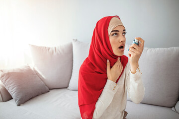 Muslim woman in hijab using inhaler at home, suffering breathing problem. Daily Life of a Person with Asthma. Woman is living life with chronic illness everyday and overcoming challenges with it.
