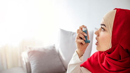Muslim woman using inhaler while suffering from asthma at home. Young woman using asthma inhaler....