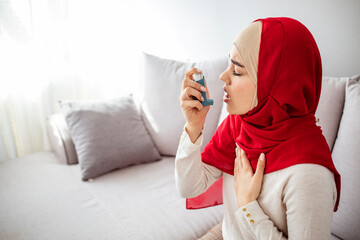 Muslim woman using inhaler while suffering from asthma at home. Young woman using asthma inhaler. Close-up of a young Muslim woman using asthma inhaler at home.
