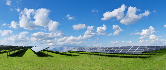 Solar power plant, blue solar panels on orange Autumn grass field under blue sky with clouds. Toned...