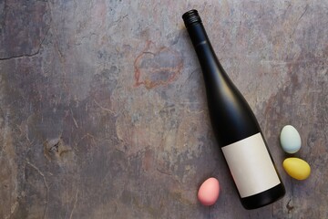 Top view of wine bottle with blank label, and colorful Easter eggs on table. Wine bottle mockup....