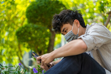 Young asian man wearing mask and using smartphone, searching or social networks concept, man typing an sms message to his friends
