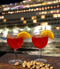 cocktail for two with orange slice to garnish with ship lights in the background