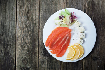 slices of salted salmon cubes cream cheese lemon mix greens on a white plate on a white background top view
