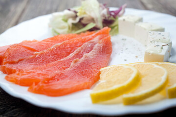 slices of salted salmon slices of cream cheese slices of lemon green salad in a white plate on a wooden background
