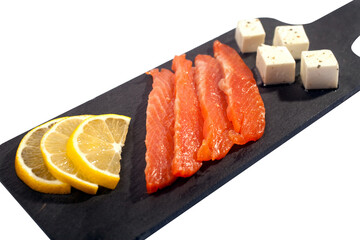 slices of salted salmon cream cheese with cubes of lemon pieces on a black shale stand on a white background