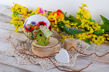A spring arrangement of flowers with a candle, a wooden bird and a birdhouse.